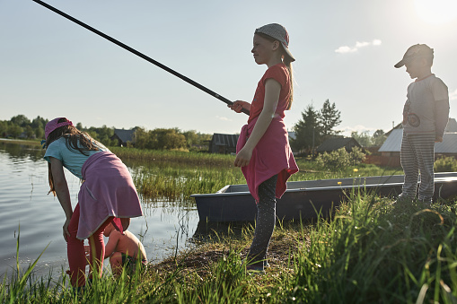Children fishing on the shore of a large lake. Girls go fishing in the summer in the village.
