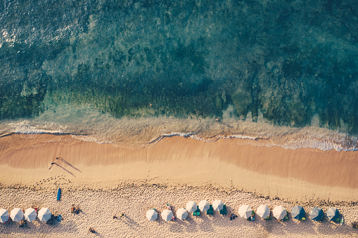 Beach scene - turquoise transparent ocean and beach umbrellas on a sandy beach. Bali beach aerial view.