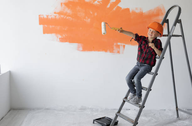 istock a boy dressed in protective orange sits on a construction ladder points with a roller to an empty space for text. 1284204389
