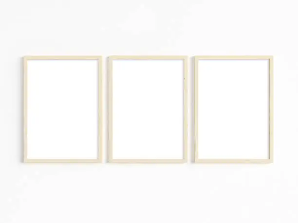A mockup of three thin A4 wooden frames with portrait orientation on a light wall. Vertical frames to display your work. 3D illustration.