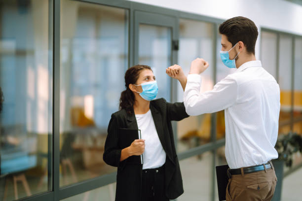 istock Two manager in protective medical masks bumping elbows while greeting each other in in modern office. 1284210786