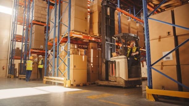 Retail Warehouse full of Shelves with Goods: Electric Forklift Truck Operator Lifts Pallet with Cardboard Box on a Shelf. People Working, Scanning Products, Using Trucks in Logistics Delivery Center almacén al por menor lleno de estantes con mercancías: operador de carretilla elevadora eléctrica levanta palés con caja de cartón en un estante. personas trabajando, escaneando productos, usando camiones en el centro de entrega de logística