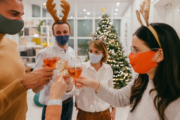 Christmas celebration in the office during Coronavirus pandemic Photo of a group of coworkers celebrating Christmas together in their office, wearing protective masks and keeping distance office christmas party stock pictures, royalty-free photos & images