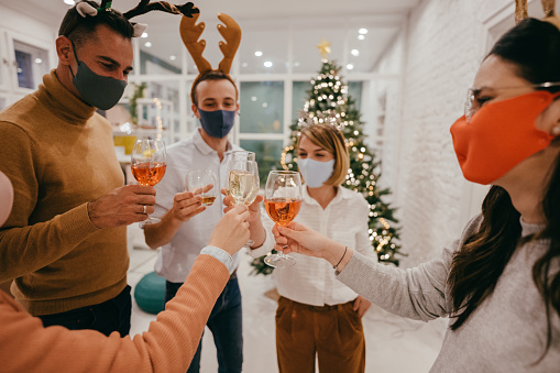 Photo of a group of coworkers celebrating Christmas together in their office, wearing protective masks and keeping distance
