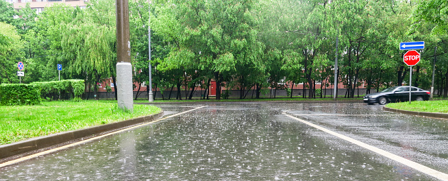 Heavy rain with hail in the city on a summer day. Paved road during heavy rain. Spray from drops and bubbles in large puddles.