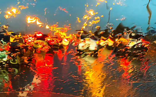 In a heavy downpour, a traffic jam formed on the road. The windshield of the car is flooded with raindrops. At night, the headlights, brake lights and dimensions of the car sparkle like Christmas lanterns. Traffic lights are reflected in puddles and car Windows