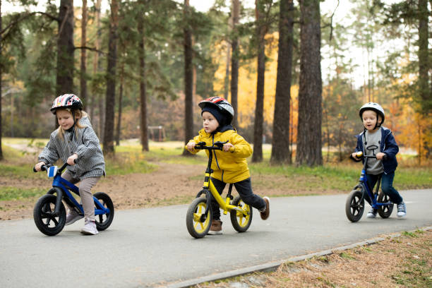 two cute little boys and adorable blond girl riding their balance bikes in park - helmet bicycle little girls child imagens e fotografias de stock