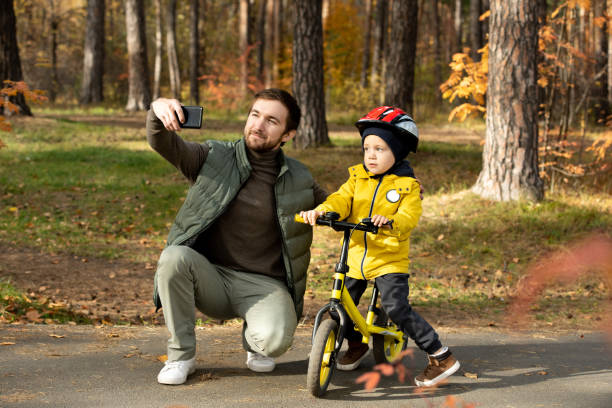 istock Happy young bearded man with smartphone making selfie with his cute little son 1284219979