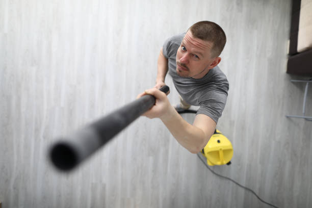 Person with protective gloves hoovering sofa with handheld vacuum cleaner