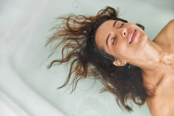 浴槽の中で水の中に横たわっている美しい若い女性 - 水に浮かぶ ストックフォトと画像