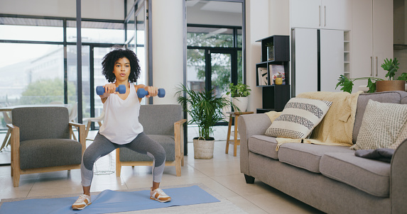 Shot of a young woman exercising with dumbbells at home