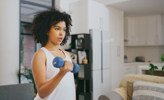 Shot of a young woman exercising with dumbbells at home