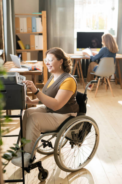 istock Happy young disable female in wheelchair pressing start button of xerox machine 1284225985