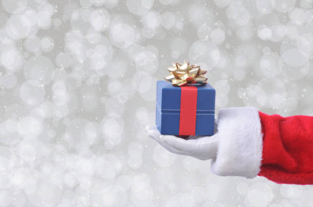 istock Santa Claus holding a blue gift box with ribbon and bow over a silver bokeh background 1284232437