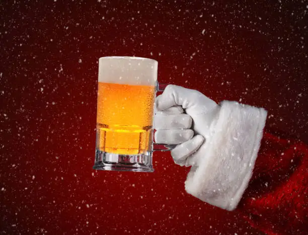 Closeup of Santa Claus holding a mug of beer. Horizontal format on a light to dark red spot background with snow effect