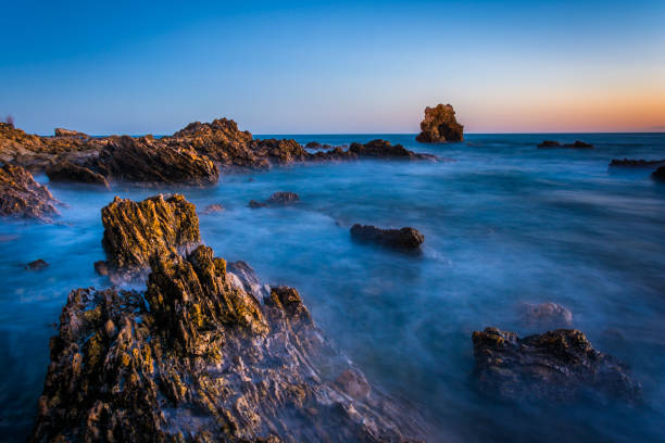 Long exposure of water and rocks at twilight, at Little Corona Beach, in Corona del Mar, California stock photo