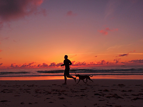 Man running along the beach with his dog during a stunning sunset.