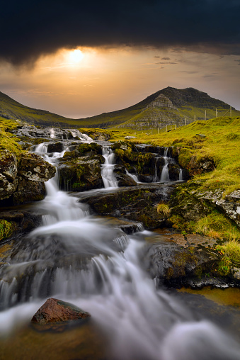Longexposure shot of a waterfall just outside of Funningur with dramatic skies above. Funningur is located on the island of Eysturoy, Faroe Islands, Denmark