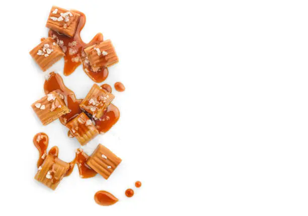 Salted caramel pieces and caramel sauce isolated on white background. Top view. Copy space.