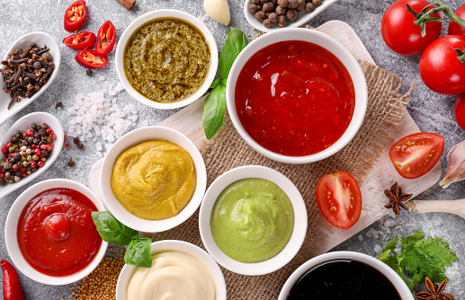 Set of sauces in small bowls and spoons on stone background. Top view.