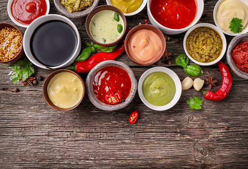 Set of sauces in small bowls on wooden background. Top view.