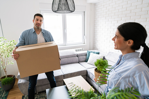 Young Caucasian couple moving into a new apartment, carrying boxes and plants.