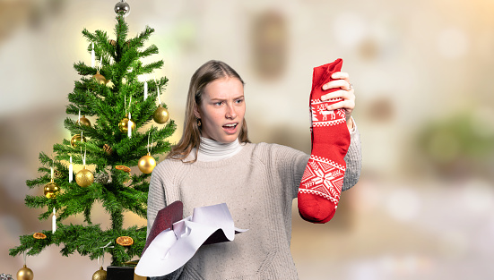 a woman in front of a Christmas tree is disappointed about her Christmas gift