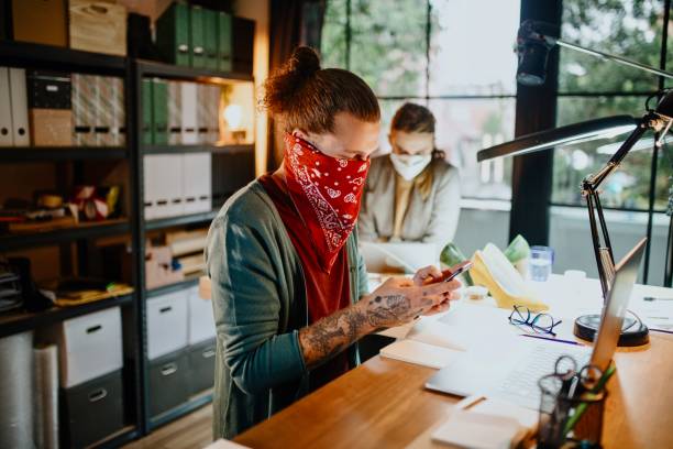 istock Young man wearing bandana mask working in office and using laptop 1284248833
