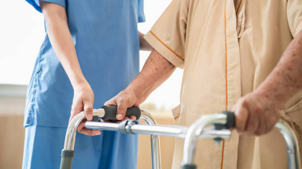 istock Close up of elderly patient hands using walking frame with nurse assistance. Medical professional or caregiver assisting senior man to walk with walker during recovery in hospital. 1284252726