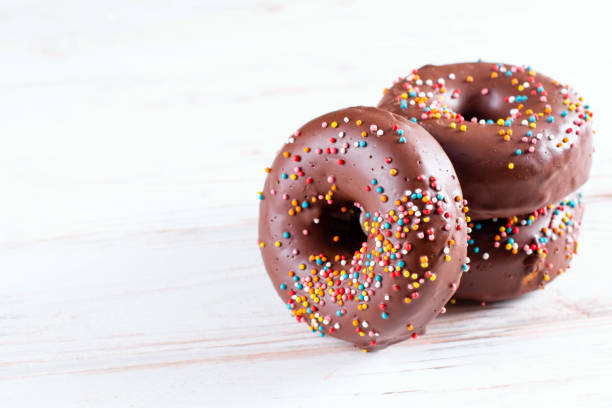 istock Delicious fresh chocolate donuts with coffee on white wooden background. Space for text 1284253140