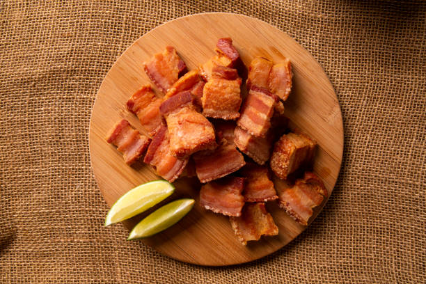 deep fried crispy pork belly served with two half lemon on the table. - pancetta imagens e fotografias de stock