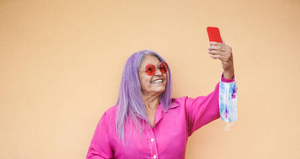 istock Hipster grandmother enjoy technology and taking a selfie with smartphone while wearing surgical face mask on her wrist 1284263755