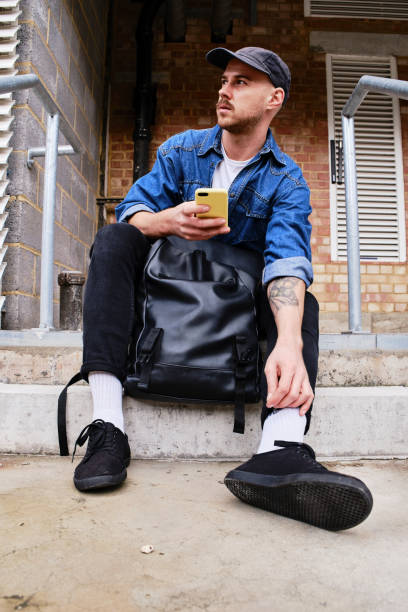 istock Unrecognizable Young Man Holding His Phone While Sitting On The Street. 1284264981