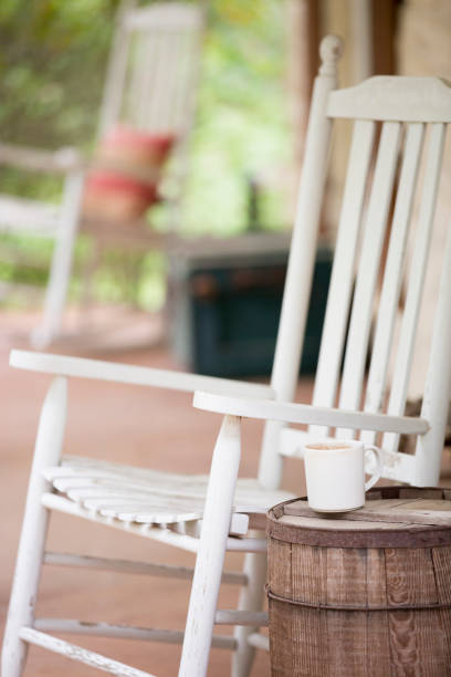 White wooden rocker on porch in rural setting.
