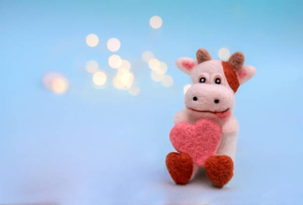 Symbol of 2021, a toy felt bull or cow with heart on a festive light blue background with bokeh, with a copy space