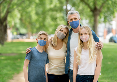 Happy family portrait wearing facemasks at the park during the COVID-19 pandemic and looking at the camera