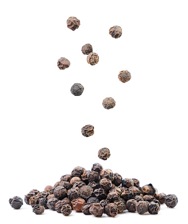 Black peppercorns falling on a pile close-up on a white background. Isolated