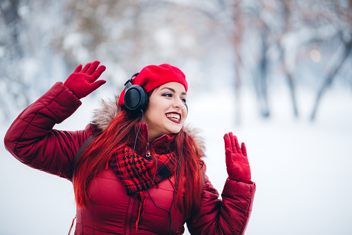 Young beautiful woman in listening music over headphones in a snow covered park.