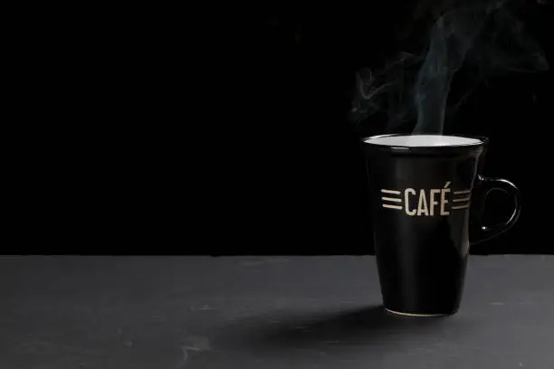Close-up on a coffee cup on a slate against a black background with copy space.