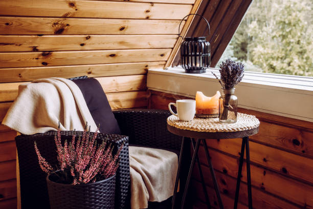 cute autumn hygge home decor arrangement. tiny wooden cabin balcony with heather flowers in pot, lavender in bottle vase, candlelight flame, soft plaid waiting on comfortable garden furniture chair. - fake rattan imagens e fotografias de stock