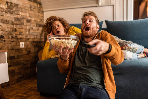 Shocked young couple watching a movie at home. Shocked young ginger couple watching an event on tv. haunted house stock pictures, royalty-free photos & images