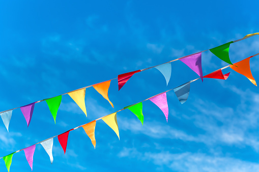 Colorful bunting flags in the wind. Festive background for holidays, anniversary, celebration. Multi-colored flag garland against a blue saturated sky