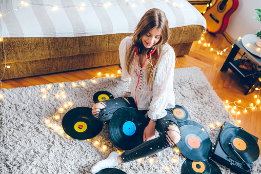 Young beautiful teenage girl listening old records in living room in lockdown.