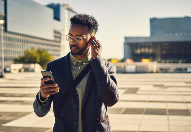 Time for some tunes Cropped shot of a handsome young businessman using his cellphone while out in the city in ear headphones stock pictures, royalty-free photos & images