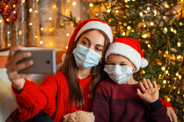 istock Brother and sister congratulates their relatives on Christmas using video call. Distance celebrating of Christmas and new 2021 Year because of coronavirus pandemic 1284285263
