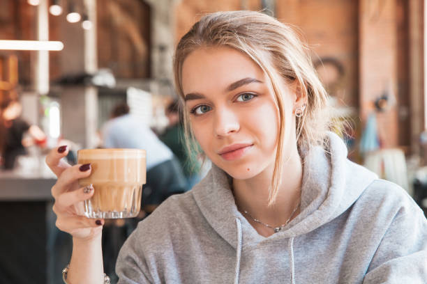 Girl holds a glass of flat white coffee. Close-up Young blond beautiful European girl holds a glass of flat white coffee. Close-up photo with selective soft focus cute 15 year old girls stock pictures, royalty-free photos & images