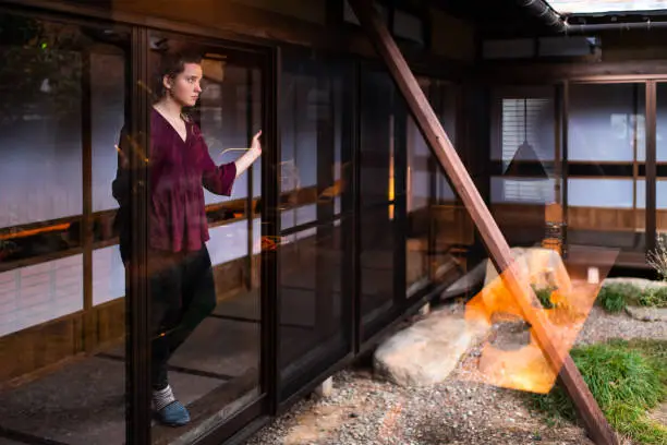Young woman standing looking through window sliding door on small inside indoor Japan Japanese traditional garden with gravel stone rocks in house