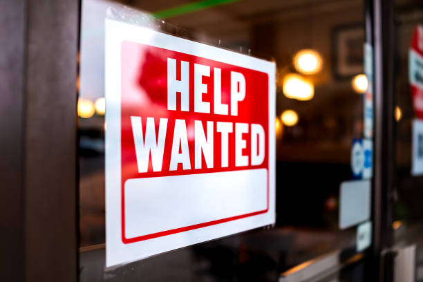 Sign text closeup for help wanted with red and white colors by entrance to store shop business building during corona virus covid 19 pandemic Sign text closeup for help wanted with red and white colors by entrance to store shop business building during corona virus covid 19 pandemic help wanted sign stock pictures, royalty-free photos & images