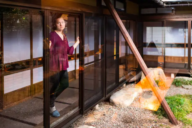 Japan with young woman standing looking through window sliding door on small indoor Japanese traditional garden with gravel stone rocks in house