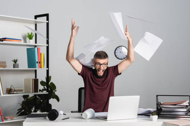 istock Stressed businessman screaming while throwing papers near laptop on office table 1284296889